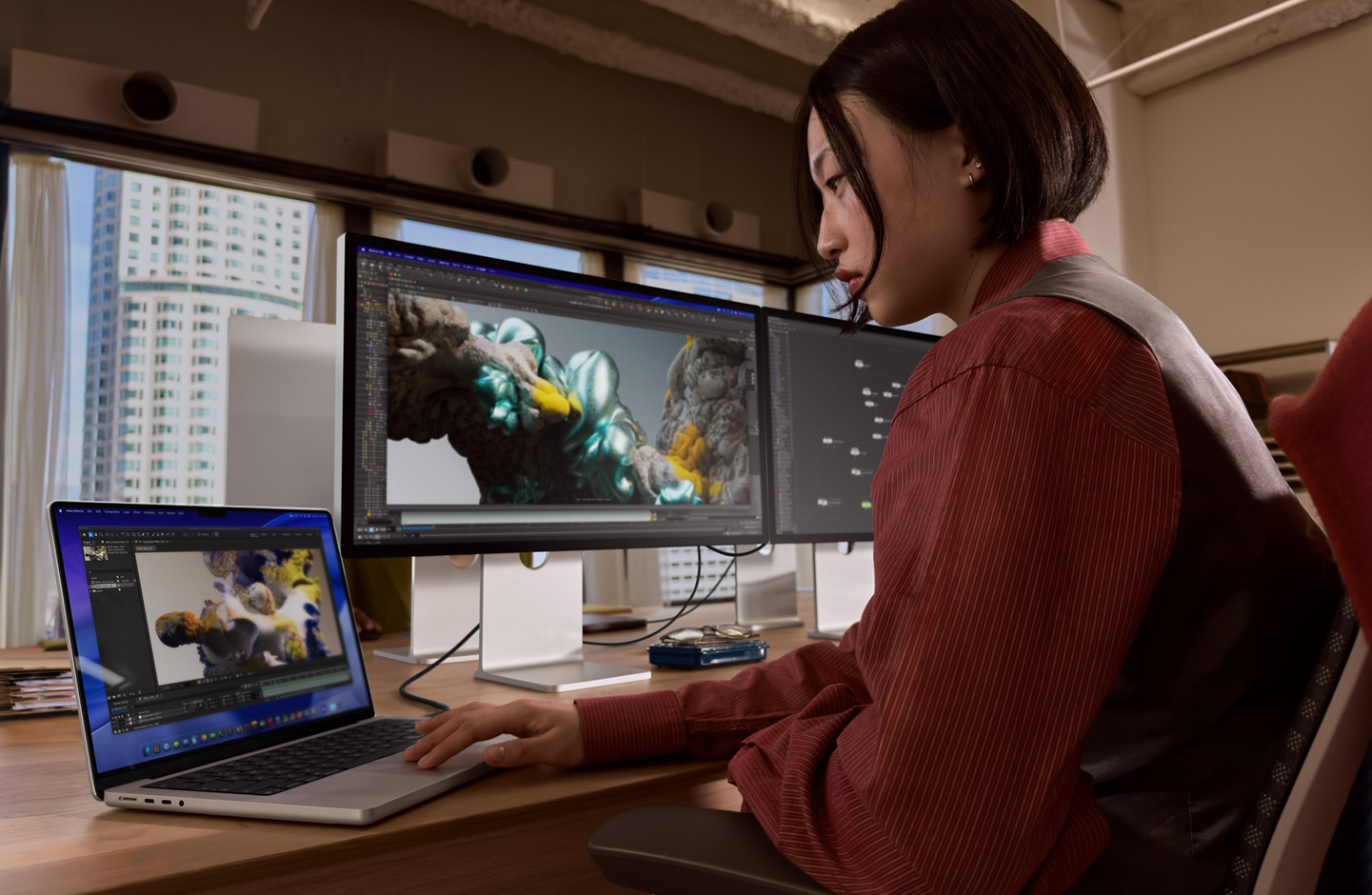 Una persona en una oficina trabaja en un portátil MacBook conectado a un Studio Display XDR mediante un puerto Thunderbolt 5