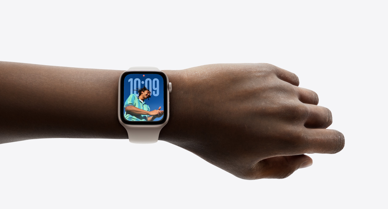 Primo piano di un Apple Watch color oro rosa con cinturino in gomma al polso di una persona, che mostra l’ora nel nuovo design Liquid Glass