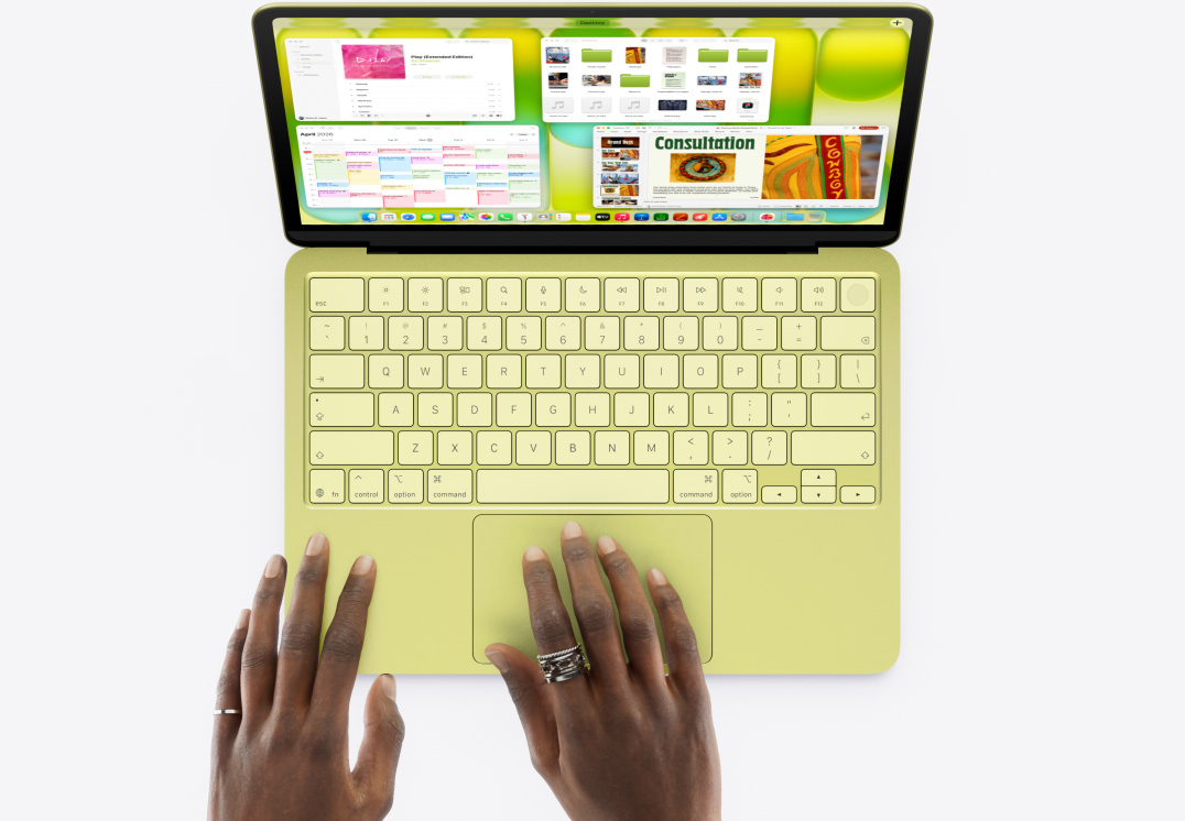MacBook Neo, culoare Galben citric, mâna unei persoane pe trackpad, mai multe ferestre deschise, inclusiv aplicațiile Muzică, Calendar și Microsoft PowerPoint